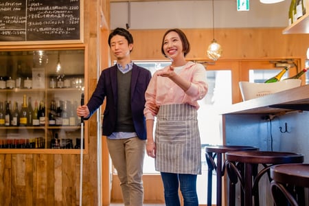 白杖を持っている人を、店員が案内する様子