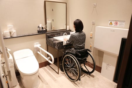 写真　多目的トイレの手洗い場の高さが問題ないか、車椅子ユーザーが調査している写真