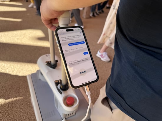【写真】AIスーツケースに設置されているスマートフォンに表示される文字。その文字が視覚障害者がつけている専用のイヤフォンに読み上げられる。