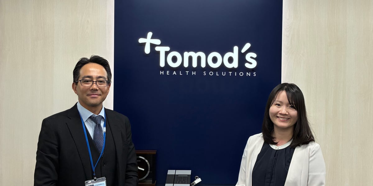 （写真）株式会社トモズのロゴがあるエントランスで撮影。インタビューに対応いただいた2名の方
