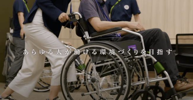 車いすに乗っている人をサポートしている写真とキャッチコピーあらゆる人が働ける環境づくりを目指す