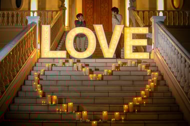 【写真】レズビアンのカップルが、LOVEと書かれたライトアップの後ろで見つめあう様子。LOVEの前には蝋燭でハートマークが作られている。