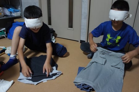 写真　アイマスクをして服を畳む小学生二人