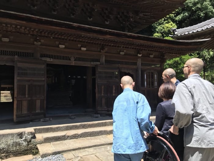 写真　階段を乗り越えるため岸田の車いすを持ち上げ和尚さんたち