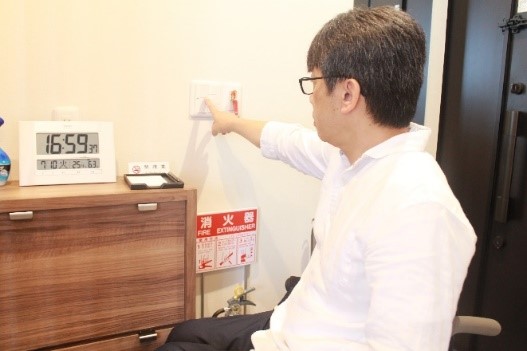 画像　車椅子ユーザーが照明スイッチを押す様子